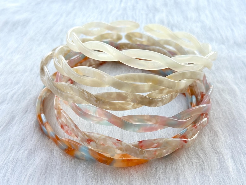 Puede incluir: Un conjunto de cuatro diademas de pl&aacute;stico trenzadas en tonos blancos, crema y melocot&oacute;n.