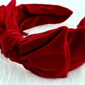 Puede incluir: Una diadema de terciopelo rojo oscuro con un dise&ntilde;o de lazo anudado. La diadema es de color liso y parece suave y afelpada. El accesorio es probablemente para peinar el cabello.