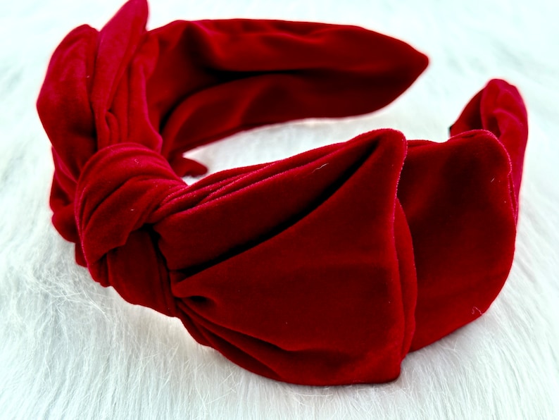 Puede incluir: Una diadema de terciopelo rojo oscuro con un dise&ntilde;o de lazo anudado. La diadema es de color liso y parece suave y afelpada. El accesorio es probablemente para peinar el cabello.