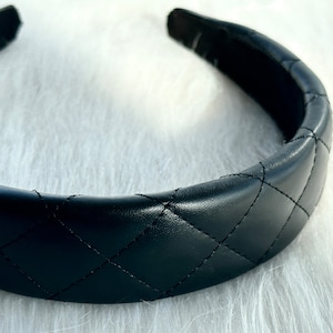 May include: A black quilted headband with a wide, padded band. The headband is made of faux leather and has a diamond-shaped quilting pattern.