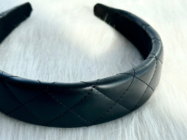 May include: A black quilted headband with a wide, padded band. The headband is made of faux leather and has a diamond-shaped quilting pattern.