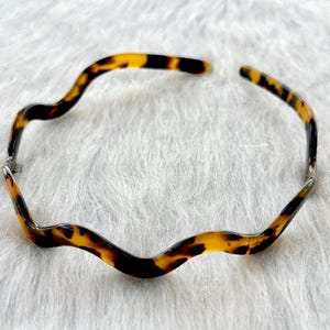 Puede incluir: Una diadema de carey con un diseño ondulado. La diadema está hecha de plástico y tiene un acabado liso.