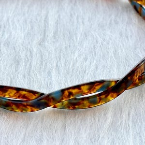 Puede incluir: Una diadema de carey marr&oacute;n y azul con un dise&ntilde;o trenzado.