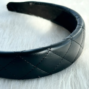 May include: A black quilted headband with a wide, padded band. The headband is made of faux leather and has a diamond-shaped quilting pattern.