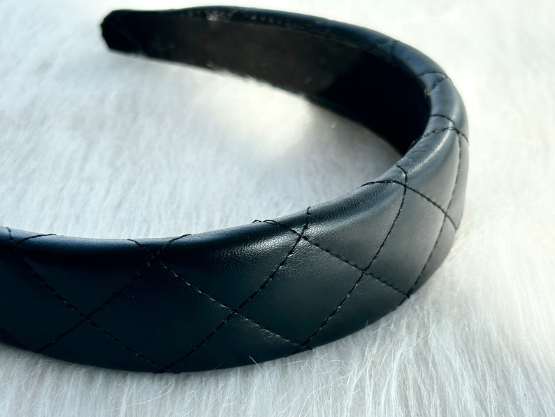 May include: A black quilted headband with a wide, padded band. The headband is made of faux leather and has a diamond-shaped quilting pattern.