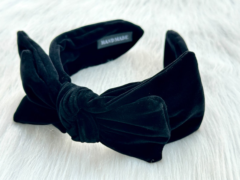 Puede incluir: Diadema de terciopelo negro con lazo anudado. La diadema es ancha y acolchada, con una etiqueta que dice "HANDMADE". Accesorio de moda para peinados y estilo.