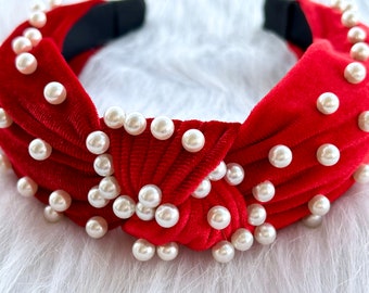May include: Red velvet headband with a knotted design and white pearl embellishments.