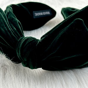 Puede incluir: Una diadema de terciopelo verde oscuro con un dise&ntilde;o de lazo anudado. La diadema est&aacute; hecha de un material suave y afelpado y presenta una peque&ntilde;a etiqueta que dice "HAND MADE". El accesorio est&aacute; dise&ntilde;ado para peinar el cabello.