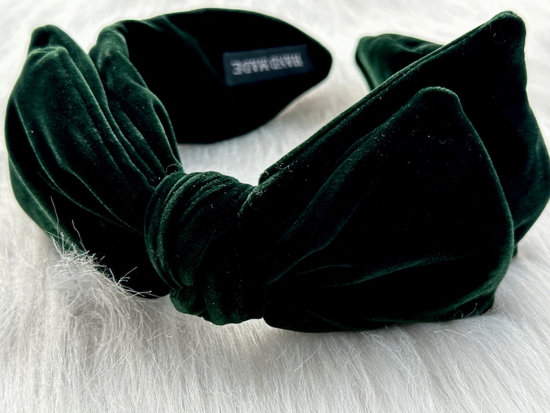 Puede incluir: Una diadema de terciopelo verde oscuro con un dise&ntilde;o de lazo anudado. La diadema est&aacute; hecha de un material suave y afelpado y presenta una peque&ntilde;a etiqueta que dice "HAND MADE". El accesorio est&aacute; dise&ntilde;ado para peinar el cabello.