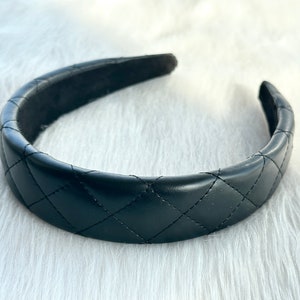 May include: A black quilted headband. The headband is made of a soft, faux leather material and has a classic quilted design.