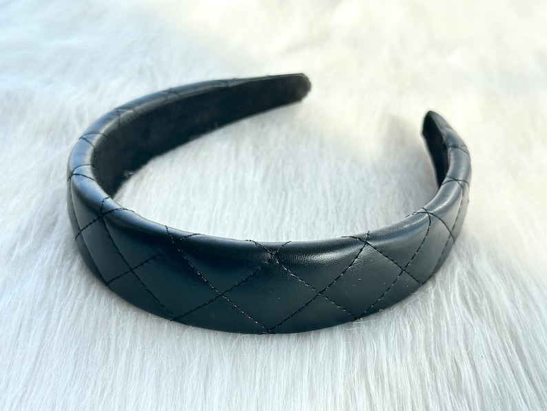 May include: A black quilted headband. The headband is made of a soft, faux leather material and has a classic quilted design.