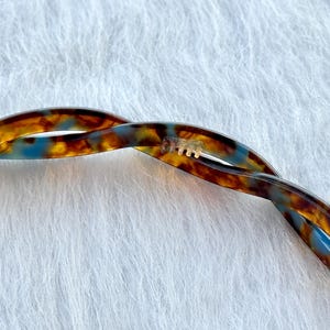 Puede incluir: Una pinza para el pelo de carey marr&oacute;n y azul con un dise&ntilde;o retorcido.