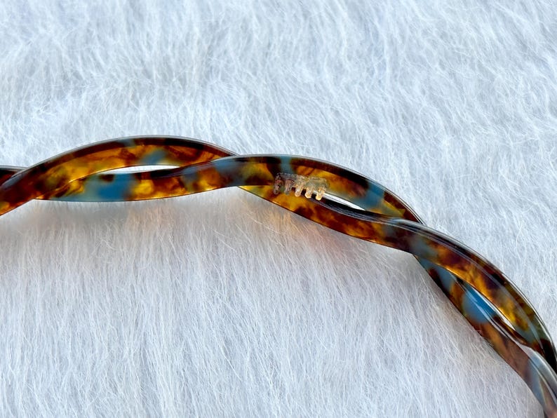 Puede incluir: Una pinza para el pelo de carey marr&oacute;n y azul con un dise&ntilde;o retorcido.