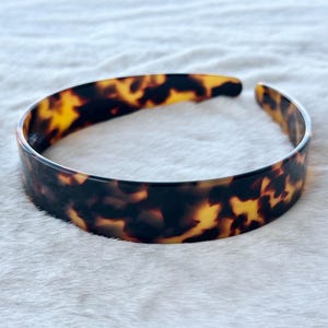 Peut inclure: Un serre-tête en écaille de tortue avec une finition brillante. Le serre-tête est de couleur marron foncé avec des reflets jaunes et ambrés. Le design ouvert est visible.