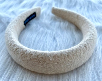May include: A thick, cream-colored headband made of a soft, fuzzy material. The headband is wide and has a slightly textured surface.