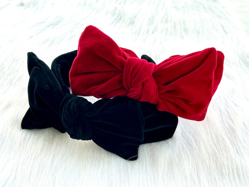 Puede incluir: Dos diademas de terciopelo con grandes lazos. Una es de color rojo intenso, la otra verde oscuro. Las diademas est&aacute;n sobre un fondo blanco y esponjoso. Estos accesorios son adecuados para diversas ocasiones.
