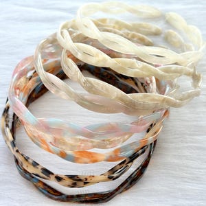 Puede incluir: Un conjunto de seis diademas de pl&aacute;stico trenzadas en varios colores y patrones, incluyendo blanco, marr&oacute;n y rosa.