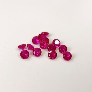 Może przedstawiać: Grupa 14 okrągłych, fasetowanych, różowych rubinów na białym tle.