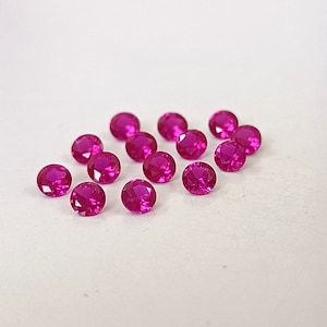 May include: A group of 15 round, pink gemstones. The gemstones are arranged in a semi-circle pattern on a white surface.