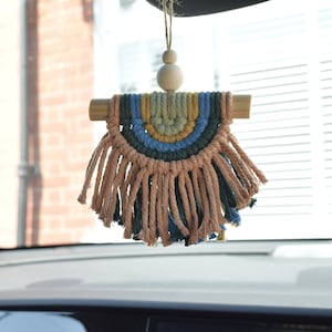 Könnte beinhalten: Ein Regenbogenfarbener Makramee-Anhänger für das Auto mit einer Holzperle und Quasten, die an einem Holzstab hängen.