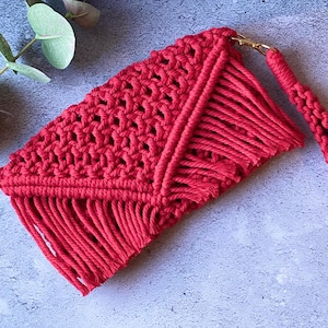 May include: A red crocheted clutch bag with a long fringe and a gold metal clasp. The bag has a matching red crocheted strap.