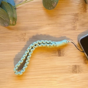 Op de afbeelding: Een lichtgroen gevlochten telefoonkoord met een kleine metalen ring aan het ene uiteinde.