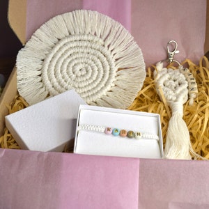 May include: A gift box filled with handmade items, including a white macrame coaster, a white macrame keyring with the name "KAREN" on it, a white beaded bracelet with colourful beads spelling "KAREN", and a white box.