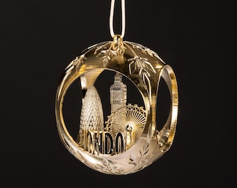 May include: A gold-colored Christmas ornament with a London theme. The ornament features cut-out designs of the Gherkin, Big Ben, and the London Eye, with the word "LONDON" in the center. The ornament hangs from a white string.