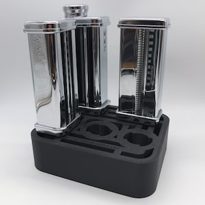 May include: A black foam stand with the text "COOP-TRUEGER.COM" holds three silver pasta roller attachments.