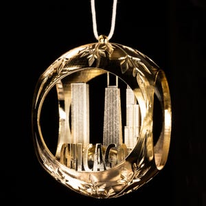 May include: A gold-colored Christmas ornament featuring the Chicago skyline. The ornament has a circular frame with floral detailing and the city name. The skyline includes iconic skyscrapers, suspended within the frame.
