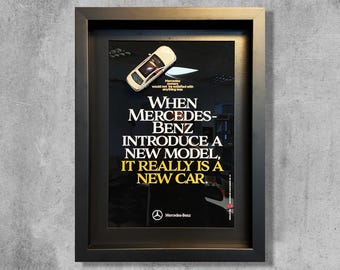 May include: A framed black and white poster with a white toy car on top. The poster has the text "When Mercedes-Benz introduce a new model, it really is a new car." and the Mercedes-Benz logo at the bottom.