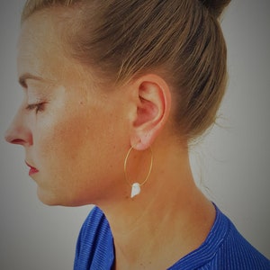 Peut inclure: Boucles d'oreilles créoles dorées avec un pendentif en forme de coquille blanche.