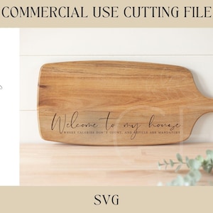 Puede incluir: Una tabla de cortar de madera con el texto "Bienvenido a mi casa, donde las calorías no cuentan y los derrames son obligatorios" grabado en ella.