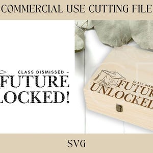 May include: A wooden box with a brown inscription that reads "Class Dismissed - Future Unlocked!" with a graduation cap graphic. The box is sitting on a white surface with green leaves in the background.