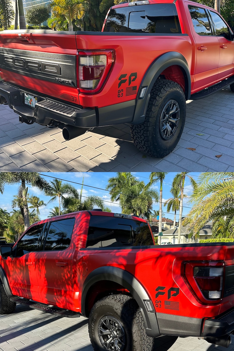 May include: A red Ford F-150 Raptor pickup truck with black accents and a "FP" decal on the back. The truck is parked on a paved driveway with palm trees in the background.