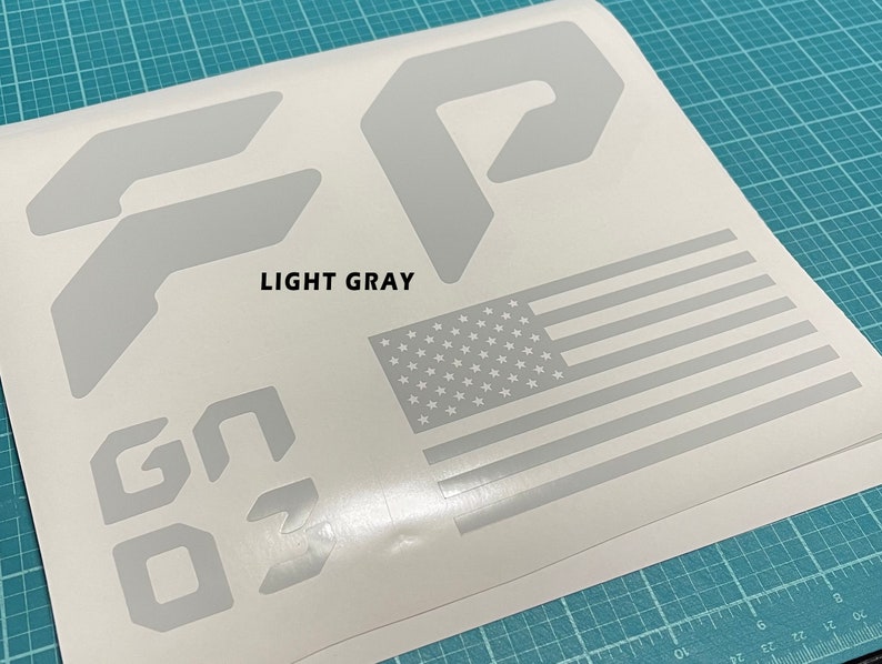 May include: A sheet of light gray vinyl decal stickers featuring the letters "GO", the number "3", and two different shapes of the letter "F". The sheet also includes a small American flag.