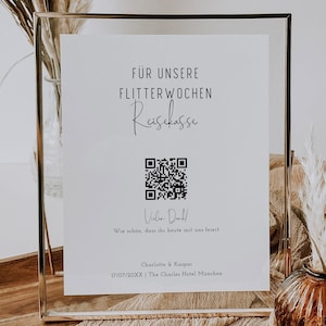 Op de afbeelding: Een wit ingelijst bord met zwarte tekst die "FÜR UNSERE FLITTERWOCHEN Reisekasse" luidt, met een QR-code en de tekst "Vielen Dank! Wie schön, dass ihr heute mit uns feiert. Charlotte & Kaspar 17/07/20XX | The Charles Hotel München".
