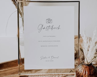 May include: A gold-framed sign with the text "Gästebuch" in cursive script. The sign also includes the text "Foto aufnehmen", "Seite aussuchen & einkleben", "Wünsche hinterlassen", "Sophie & Daniel", and "20.07.2028".