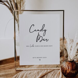 Könnte beinhalten: Ein goldfarbener Rahmen mit dem Text "Candy Bar" in Kursivschrift. Das Schild enthält auch den Text "Weil Liebe durch den Magen geht." und "Bitte bedient euch." mit einem Herzsymbol.