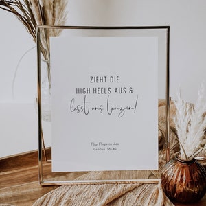 Könnte beinhalten: Ein goldfarbener Rahmen mit dem Text "ZIEHT DIE HIGH HEELS AUS & lasst uns tanzen!" und "Flip Flops in den Größen 36-42". Das Schild steht auf einer Holzoberfläche mit einem braunen Stoff und einer Vase mit getrocknetem Pampasgras.