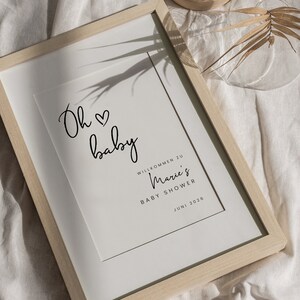 Puede incluir: Una impresi&oacute;n enmarcada con el texto "Oh baby" y un s&iacute;mbolo de coraz&oacute;n. Debajo del texto se lee "Willkommen zu Marie's Baby Shower Juni 2026".