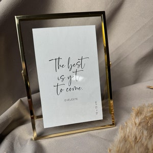 Könnte beinhalten: Ein goldfarbener Bilderrahmen mit einem weißen Passepartout und einem Schwarzweißdruck mit dem Text "The best is yet to come." Der Druck ist mit "Eveleste" signiert und der Rahmen ist 10 x 15 cm groß.