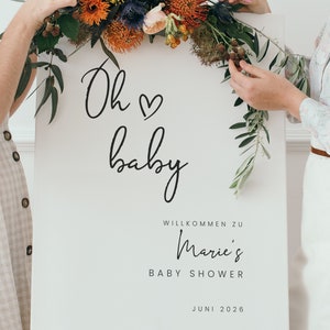 Puede incluir: Un cartel blanco con caligraf&iacute;a negra que dice "Oh baby" con un s&iacute;mbolo de coraz&oacute;n. El cartel tambi&eacute;n dice "Willkommen zu Marie's Baby Shower Juni 2026". El cartel est&aacute; decorado con una guirnalda floral de flores rojas, naranjas, amarillas y azules.