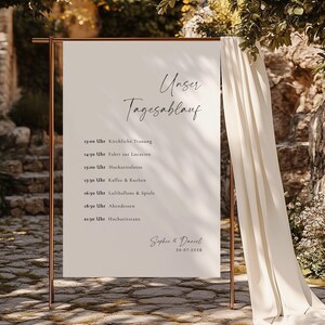 Peut inclure: Une pancarte blanche avec un cadre en cuivre, listant le programme de la journée de mariage en allemand. La pancarte indique "Unser Tagesablauf" et liste les heures de la cérémonie, des photos, de la réception et d'autres événements. La pancarte est décorée des noms du couple, Sophie & Daniel, et de la date, 20-07-2028.