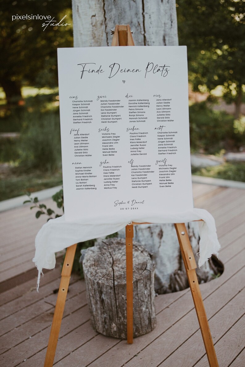 May include: A white sign with black text on an easel. The sign says "Finde Deinen Platz" which translates to "Find Your Seat" in English. The sign lists names in different categories, such as "eins", "zwei", "drei", "vier", "f&uuml;nf", "sechs", "sieben", "acht", "neun", "zehn", "elf", and "zw&ouml;lf". The sign is decorated with a heart and the date "20-07-20XX".
