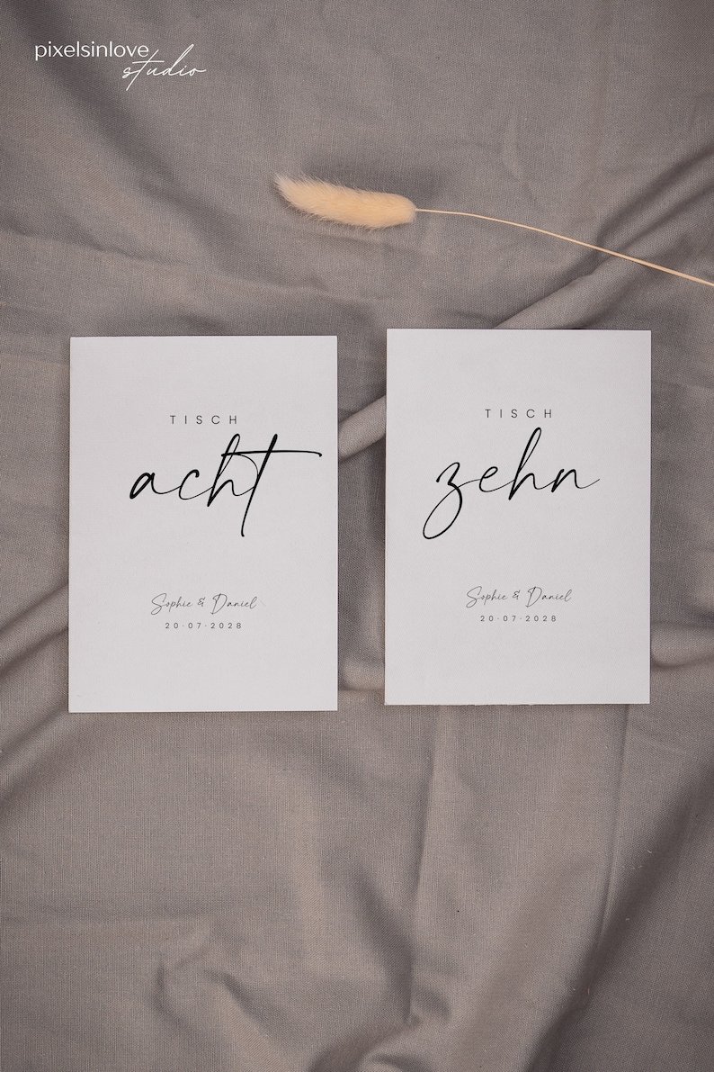 May include: Two white cards with black text. The top card says "Tisch acht" and the bottom card says "Tisch zehn". Both cards have the text "Sophie & Daniel 20.07.2028" printed on them.