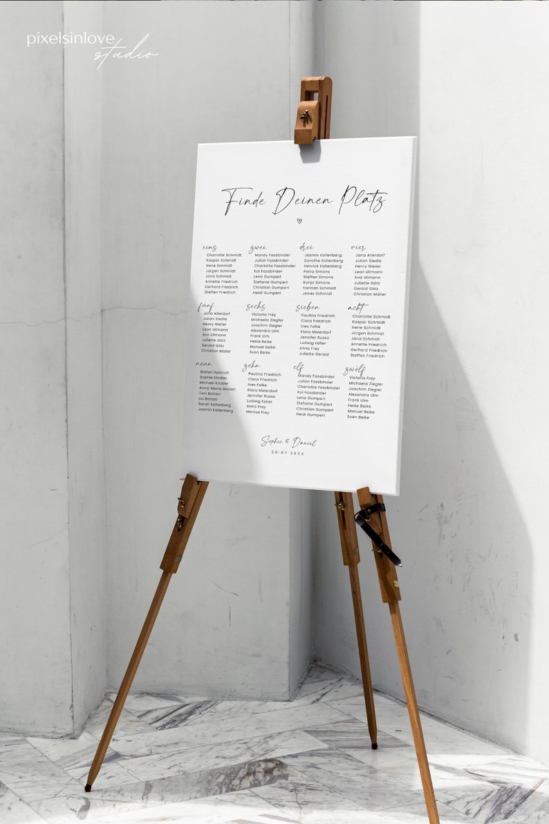 May include: A white sign with black text on an easel. The sign says "Finde Deinen Platz" and lists names under the headings "eins", "zwei", "drei", "vier", "f&uuml;nf", "sechs", "sieben", "acht", "neun", "zehn", "elf", "zw&ouml;lf". The sign is dated "20-07-20xx".