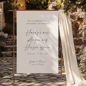 May include: A white sign with black text announcing a wedding. The text reads "Welcome to our wedding. Phones off. Eyes on. Hearts open. Start: 2:00 PM. Sophie & Daniel 20-07-2028"