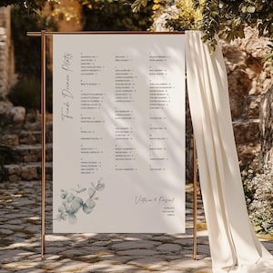 May include: A rectangular wedding seating chart sign on a copper-colored metal stand. The white sign features the text Finde Deinen Platz, a list of names with table numbers, a watercolor eucalyptus illustration, and the names Victoria & Pascal.