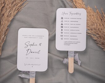 Puede incluir: Un abanico de boda blanco con un diseño en blanco y negro. El abanico tiene un mango de madera y una cinta azul claro. La parte delantera del abanico dice "Sophie & Daniel" y "20 de julio de 2028". La parte posterior del abanico tiene una lista de eventos de boda con horarios e iconos.